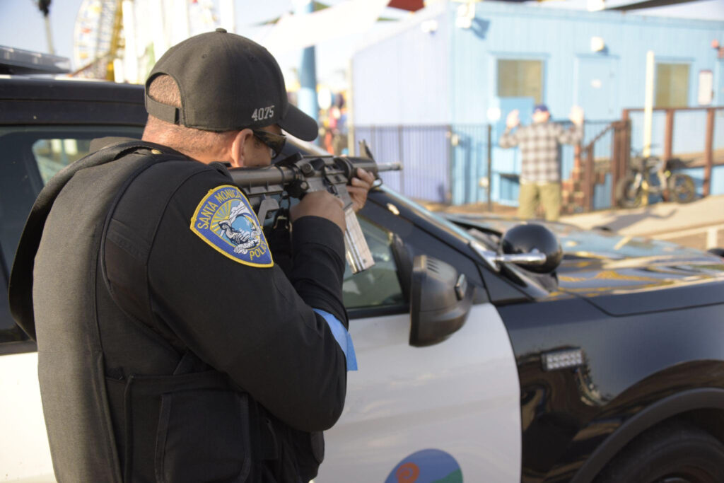 A SMPD officer keeps his weapon trained on the Pier arcade