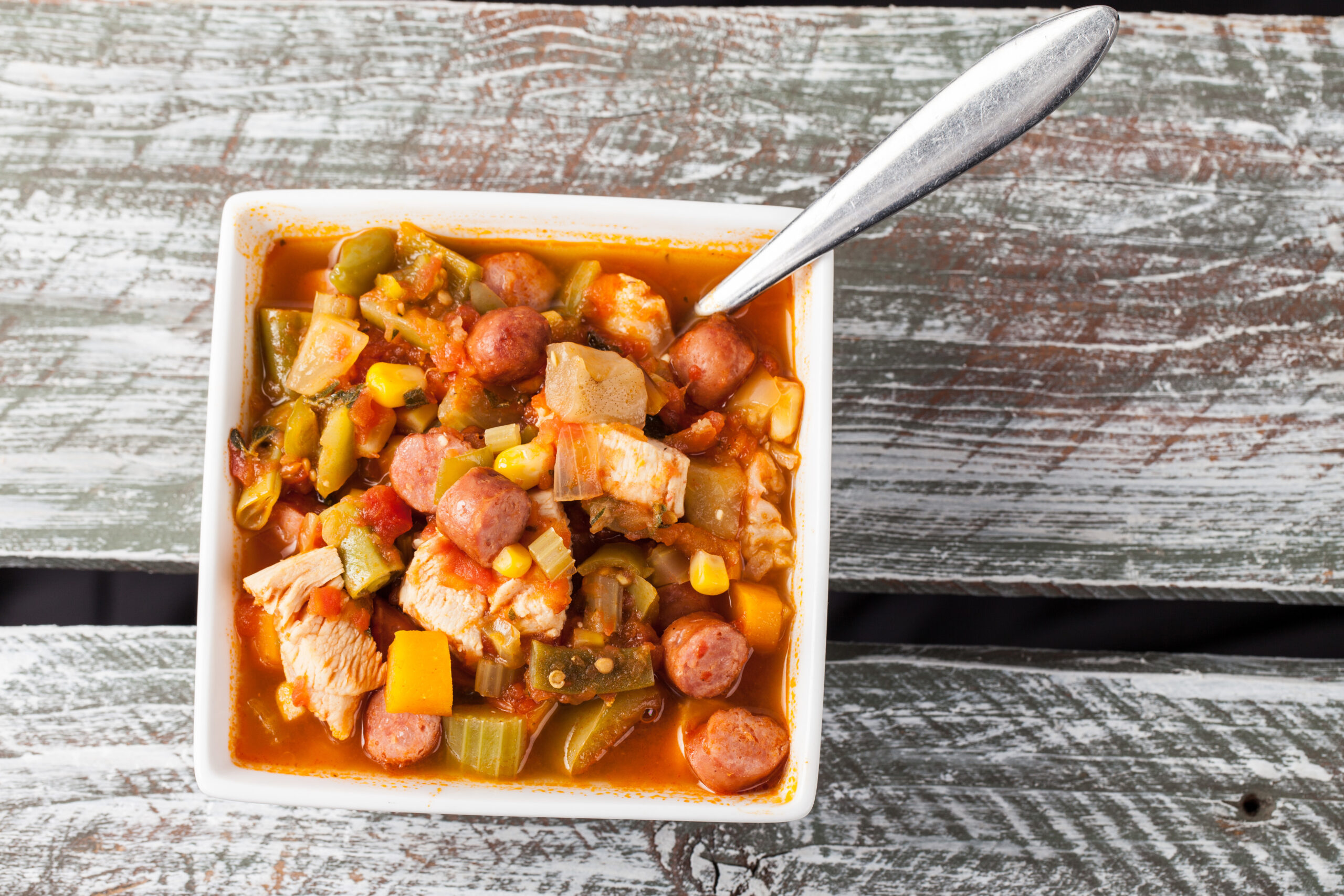 White square bowl of homemade chicken gumbo soup on a weathered