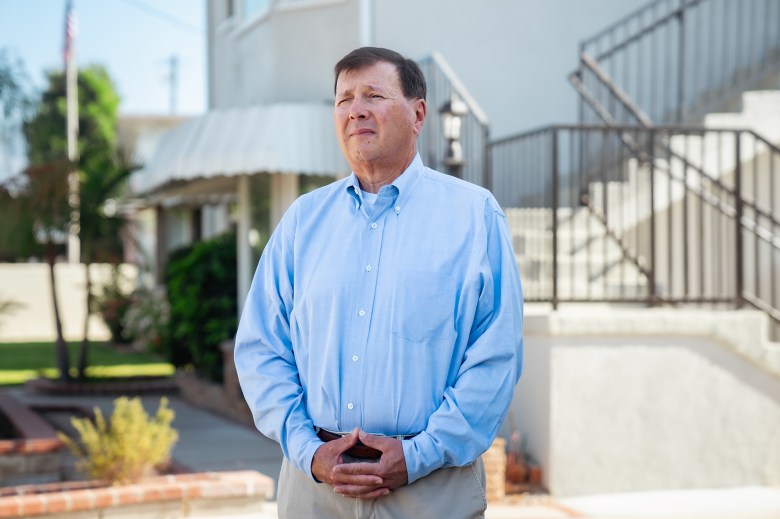 Mike Placido, wearing a light blue button-up shirt and khaki pants, stands in front of a four-unit , light white, rental property that he and his wife own and manage in San Gabriel on Aug. 12, 2024. Photo by Jules Hotz for CalMatters