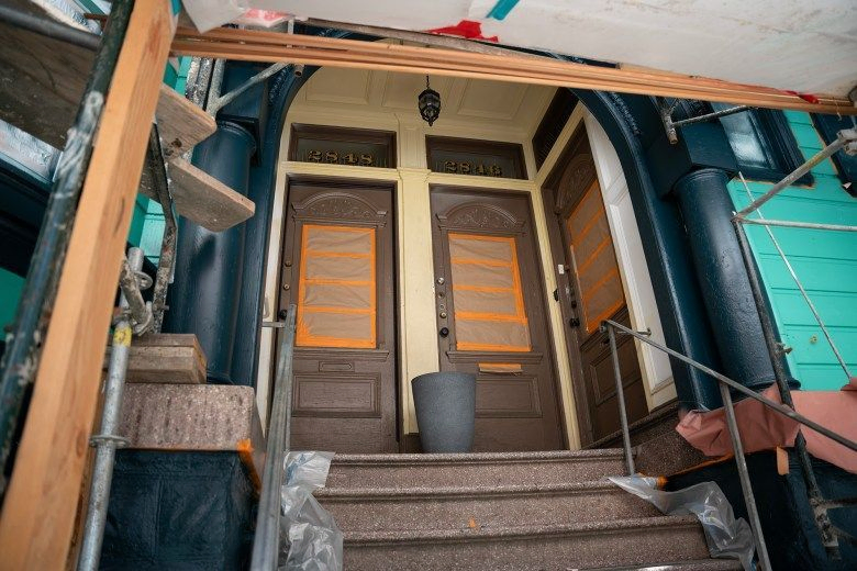 A view of the the front door of a building that's covered in a tarp and construction materials.