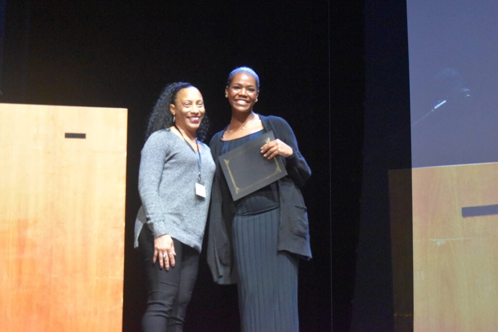 A Black female teenager receives an educational award on stage.