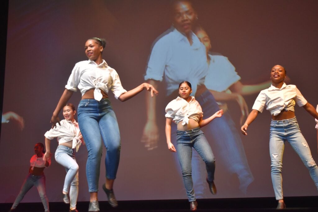 A group of Black girl teenagers dance on stage during a Martin Luther King, Jr. Day celebration.