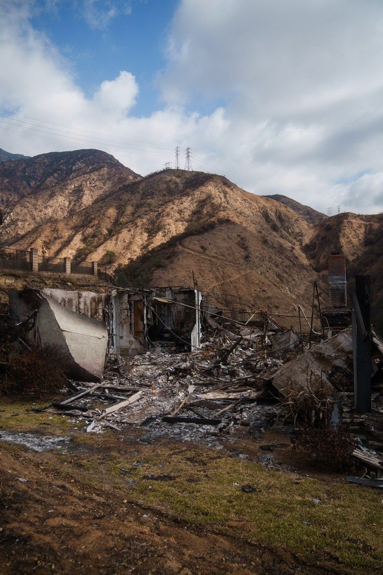 The charred remains of a house and mountainside that burned during a recent wildfire. Only one structure of the house remains standing.